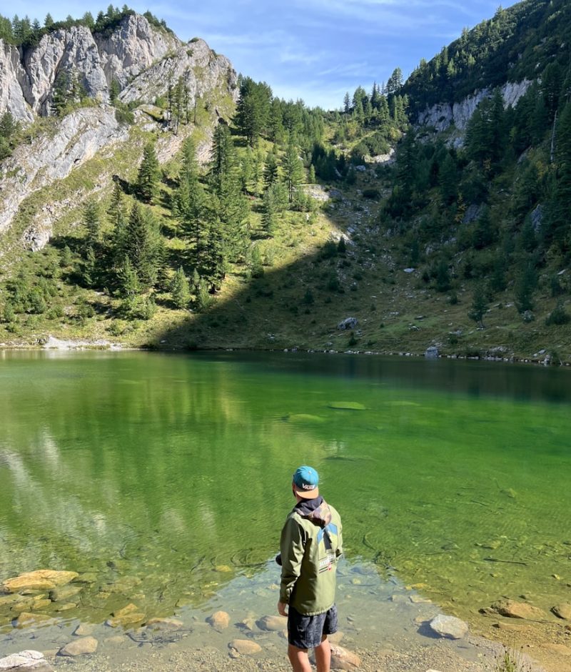 a man standing on a rock by a lake with trees and mountains in the background